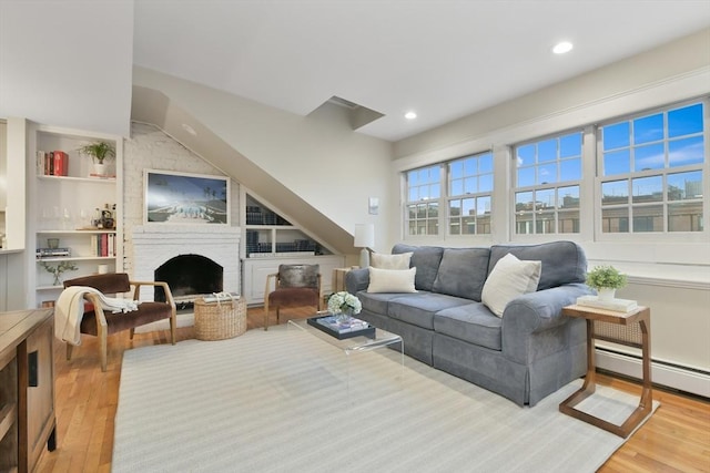 living room with light hardwood / wood-style floors, baseboard heating, built in features, and a fireplace