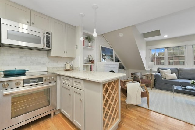 kitchen with kitchen peninsula, light hardwood / wood-style flooring, hanging light fixtures, appliances with stainless steel finishes, and light stone countertops