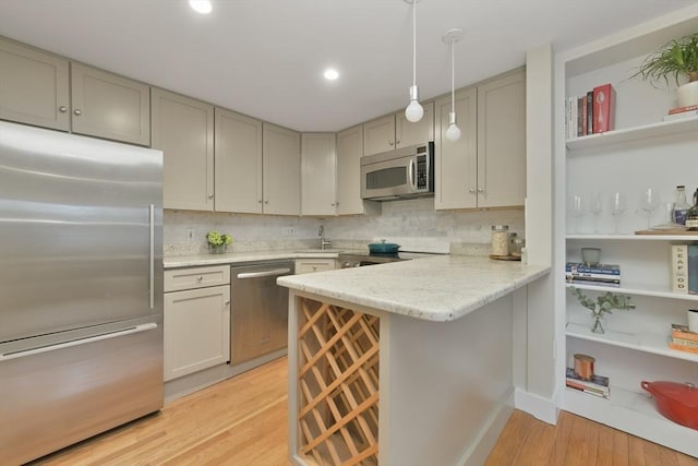 kitchen with stainless steel appliances, a kitchen breakfast bar, hanging light fixtures, kitchen peninsula, and light hardwood / wood-style flooring