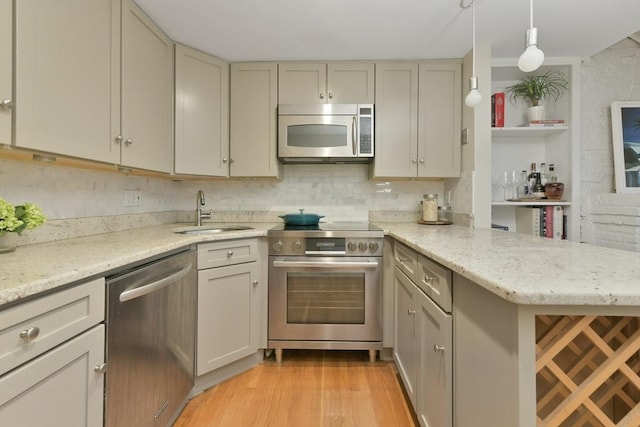 kitchen featuring appliances with stainless steel finishes, sink, light hardwood / wood-style flooring, kitchen peninsula, and pendant lighting