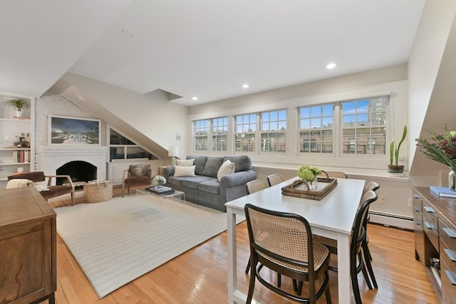 dining area featuring a fireplace, light wood-type flooring, built in shelves, and a baseboard heating unit