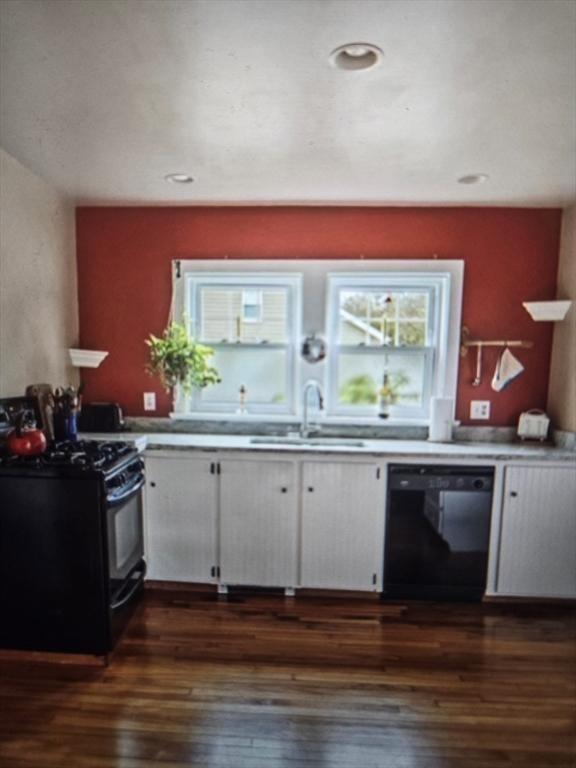 kitchen with dark wood-style flooring, light countertops, black appliances, white cabinetry, and a sink