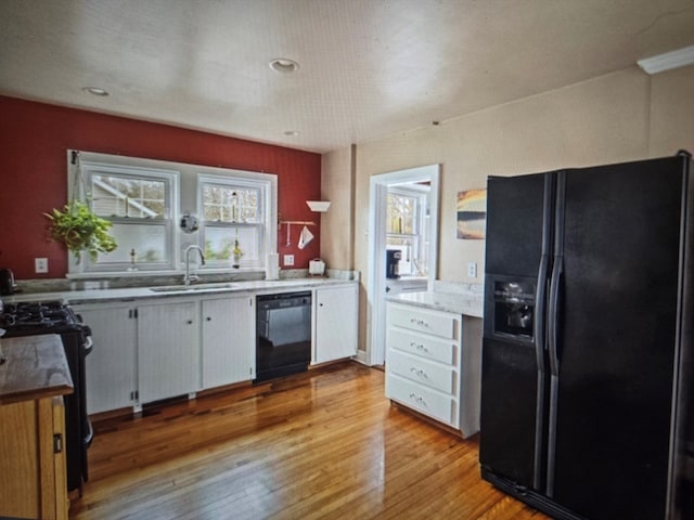 kitchen with black appliances, white cabinetry, sink, and light hardwood / wood-style floors