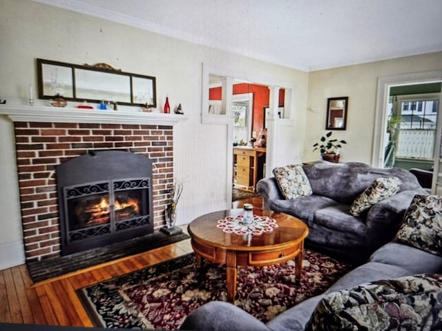 living room with wood-type flooring, crown molding, and a brick fireplace