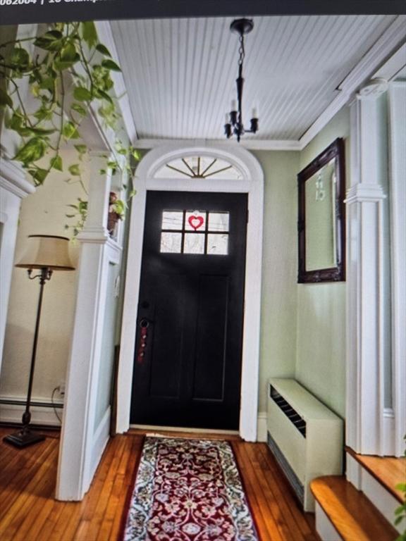 entryway with radiator, wood-type flooring, baseboard heating, a chandelier, and ornate columns