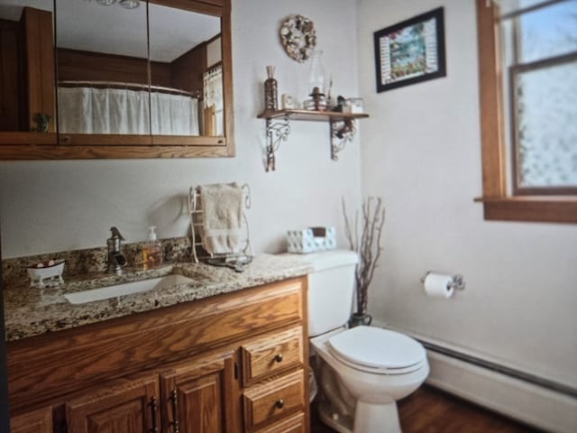 bathroom with a baseboard heating unit, vanity, toilet, and a wealth of natural light