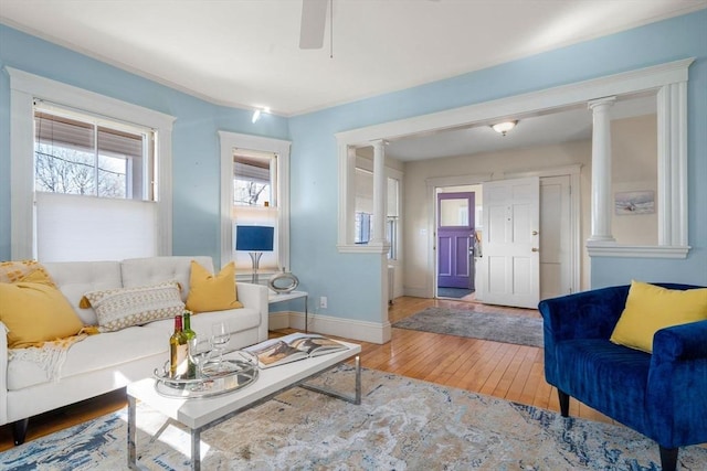 living room with decorative columns, wood-type flooring, baseboards, and ceiling fan