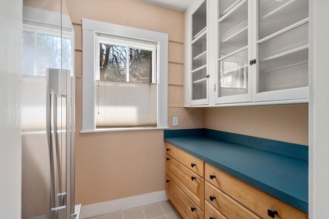 kitchen featuring light tile patterned floors, glass insert cabinets, and baseboards