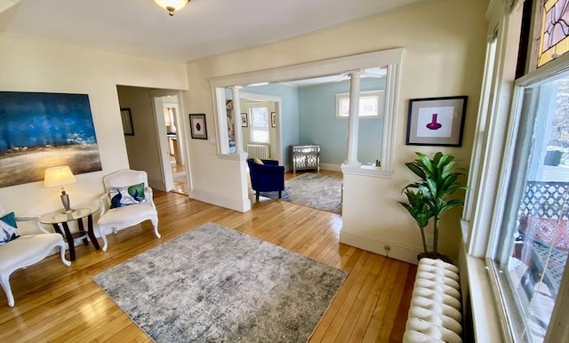 living room with light wood finished floors, radiator heating unit, baseboards, and ornate columns