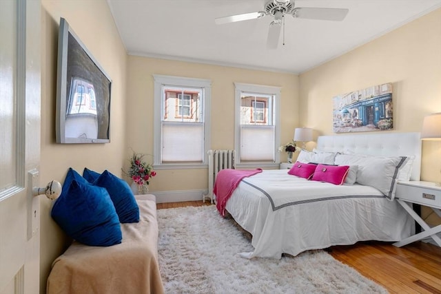 bedroom with ceiling fan, radiator, baseboards, and wood finished floors