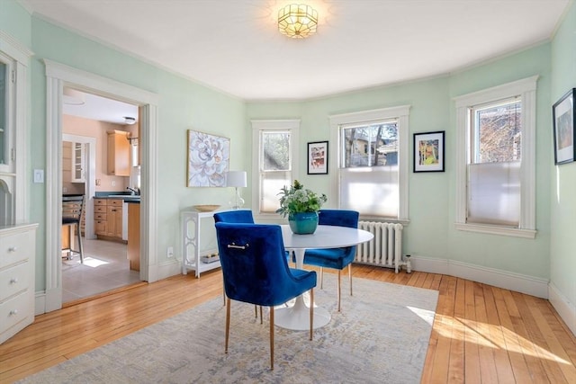 dining area featuring light wood-type flooring, radiator heating unit, baseboards, and ornamental molding