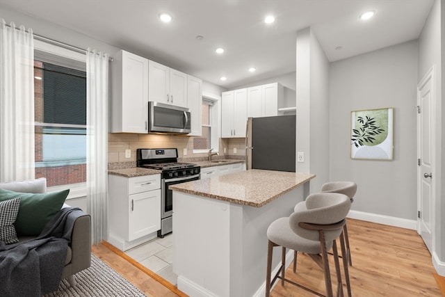 kitchen with light stone countertops, white cabinetry, stainless steel appliances, and light hardwood / wood-style flooring