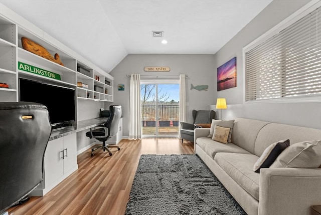 office area featuring visible vents, baseboards, vaulted ceiling, built in desk, and light wood-type flooring