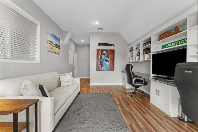 office with visible vents, baseboards, vaulted ceiling, built in desk, and wood finished floors