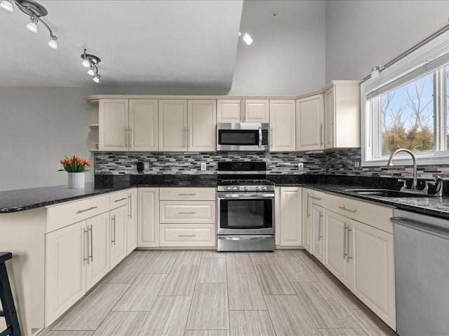 kitchen featuring a peninsula, open shelves, a sink, appliances with stainless steel finishes, and tasteful backsplash