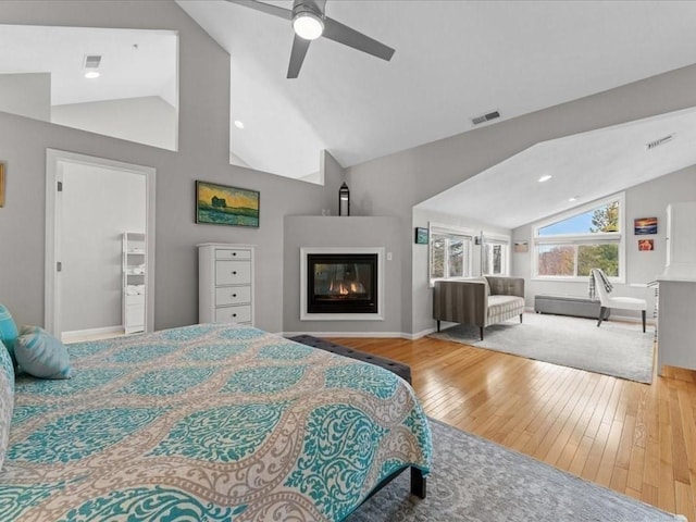 bedroom with visible vents, lofted ceiling, a glass covered fireplace, a ceiling fan, and wood-type flooring