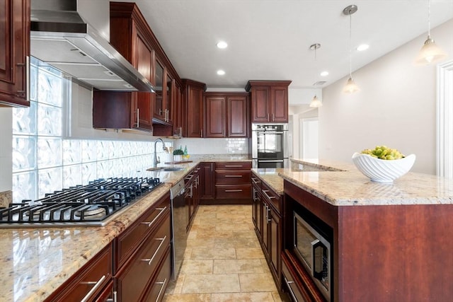 kitchen featuring appliances with stainless steel finishes, decorative light fixtures, light stone countertops, wall chimney exhaust hood, and sink