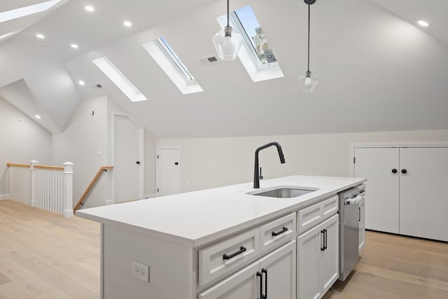 kitchen featuring lofted ceiling with skylight, sink, light hardwood / wood-style floors, hanging light fixtures, and an island with sink