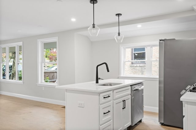 kitchen with appliances with stainless steel finishes, light wood-type flooring, sink, pendant lighting, and an island with sink