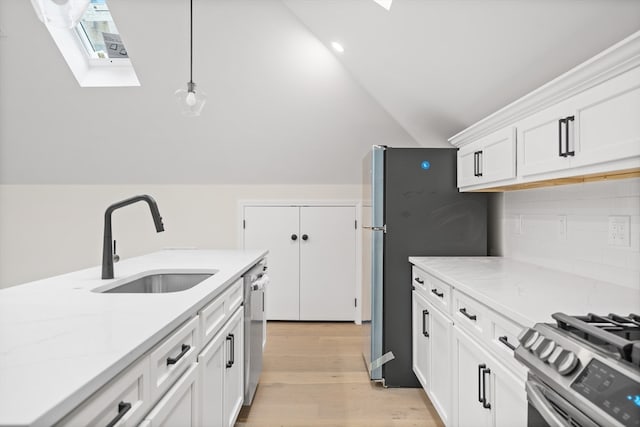 kitchen featuring white cabinetry, sink, lofted ceiling with skylight, light hardwood / wood-style floors, and decorative light fixtures