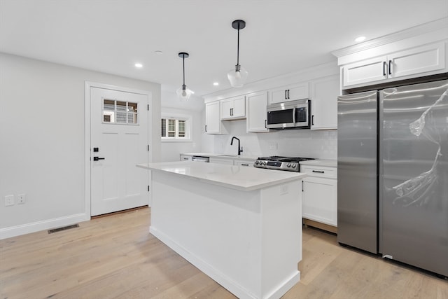 kitchen with white cabinetry, hanging light fixtures, stainless steel appliances, light hardwood / wood-style floors, and a kitchen island