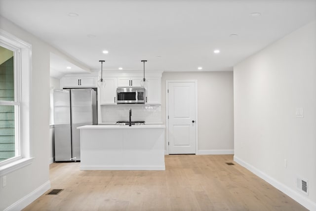 kitchen featuring stainless steel appliances, a kitchen island with sink, pendant lighting, light hardwood / wood-style floors, and white cabinetry