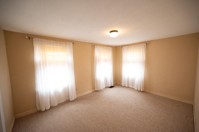 unfurnished room featuring baseboards, light colored carpet, and a healthy amount of sunlight