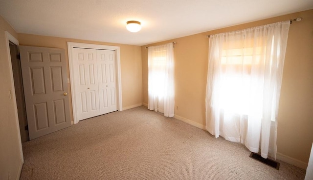 unfurnished bedroom with a closet, visible vents, light colored carpet, and baseboards