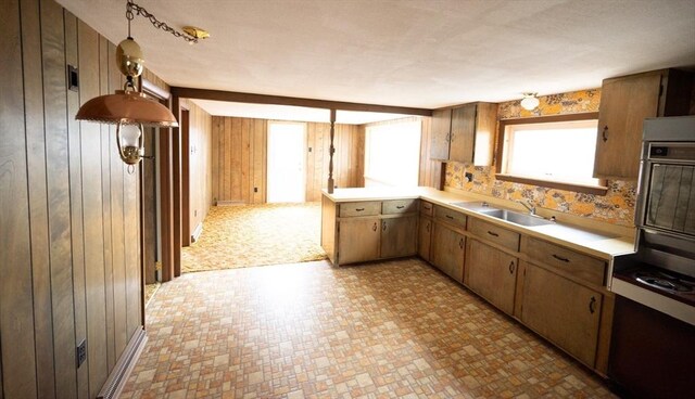 kitchen with light countertops, wood walls, light floors, wall oven, and a sink