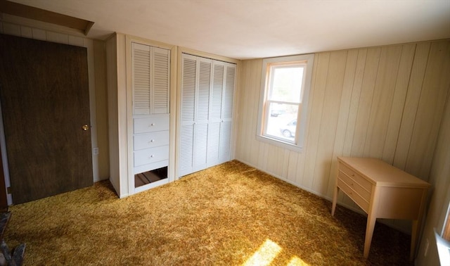 unfurnished bedroom with wooden walls, two closets, and carpet floors