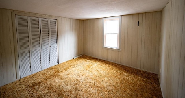 unfurnished bedroom featuring a closet, wood walls, carpet, and a baseboard heating unit