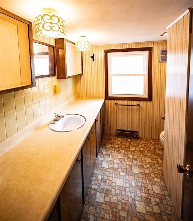 bathroom featuring toilet, a wealth of natural light, brick patterned floor, and vanity