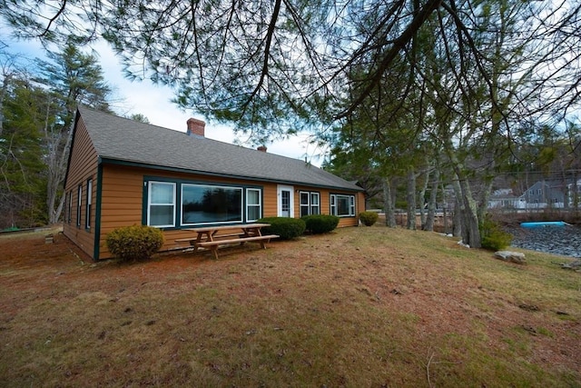 back of property with a yard, roof with shingles, and a chimney