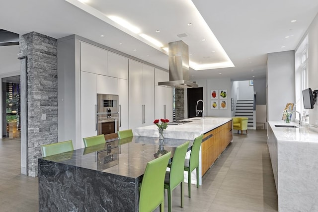 kitchen with sink, white cabinetry, a breakfast bar area, and island exhaust hood