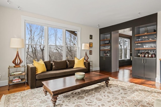 living room with bar, dark hardwood / wood-style flooring, built in shelves, and a wealth of natural light