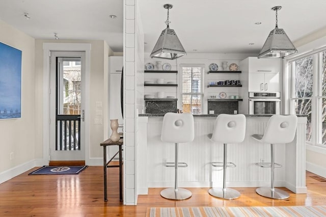 kitchen featuring stainless steel oven, white cabinets, a kitchen breakfast bar, and light hardwood / wood-style floors