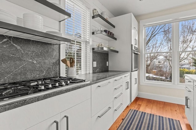 kitchen featuring white cabinetry, decorative backsplash, light hardwood / wood-style floors, stainless steel appliances, and wall chimney range hood