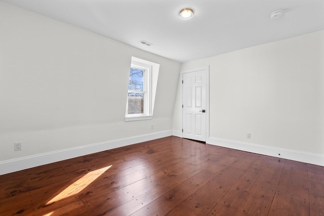 unfurnished room with dark wood-style floors, visible vents, and baseboards