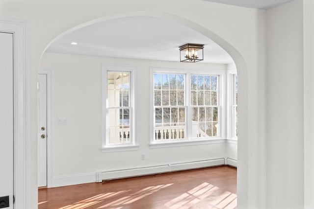 unfurnished dining area with wood finished floors, arched walkways, baseboard heating, and baseboards