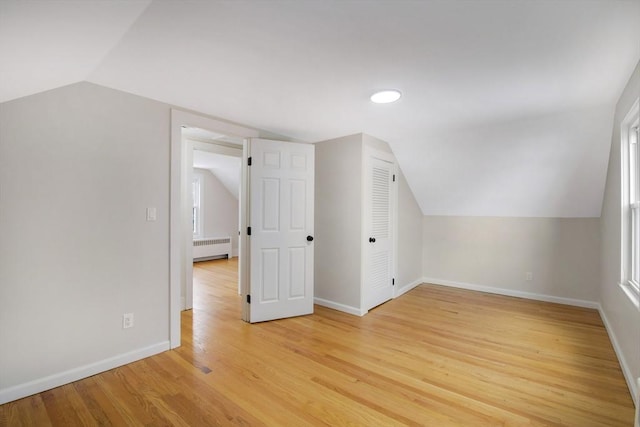 additional living space with vaulted ceiling, radiator, and light hardwood / wood-style flooring