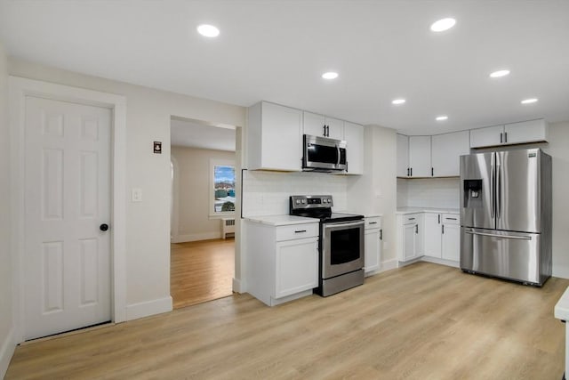 kitchen featuring tasteful backsplash, stainless steel appliances, light wood-type flooring, and white cabinets