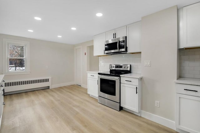 kitchen featuring radiator, stainless steel appliances, tasteful backsplash, white cabinets, and light wood-type flooring