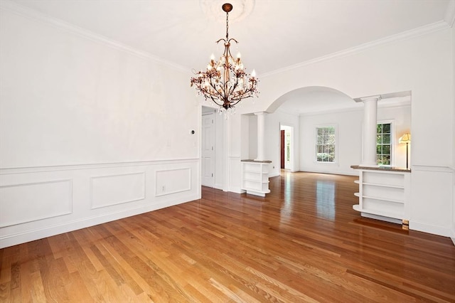 136 Howard St, Northborough, MA 01532 - unfurnished dining area featuring arched walkways, decorative columns, wood finished floors, crown molding, and a decorative wall
