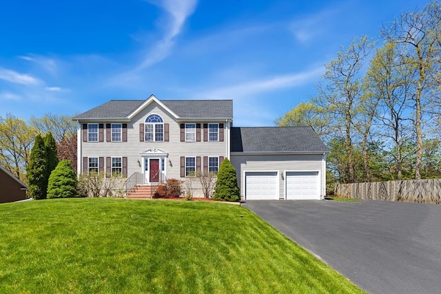 colonial-style house with an attached garage, aphalt driveway, fence, and a front yard