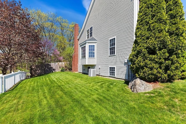 view of home's exterior featuring fence, a chimney, a lawn, and cooling unit
