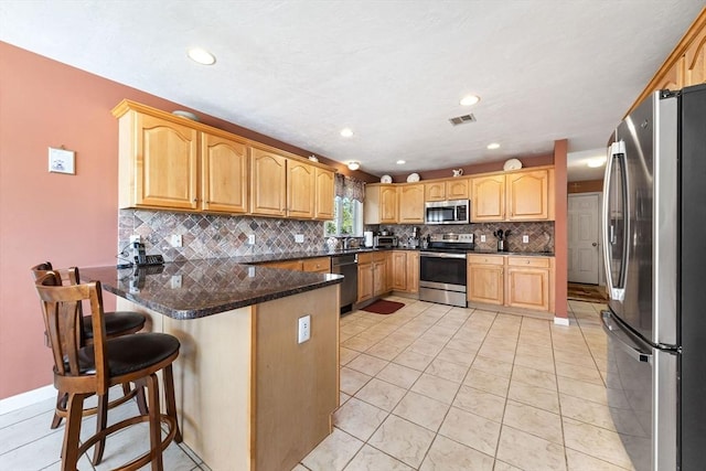 kitchen with visible vents, a peninsula, a kitchen breakfast bar, backsplash, and stainless steel appliances
