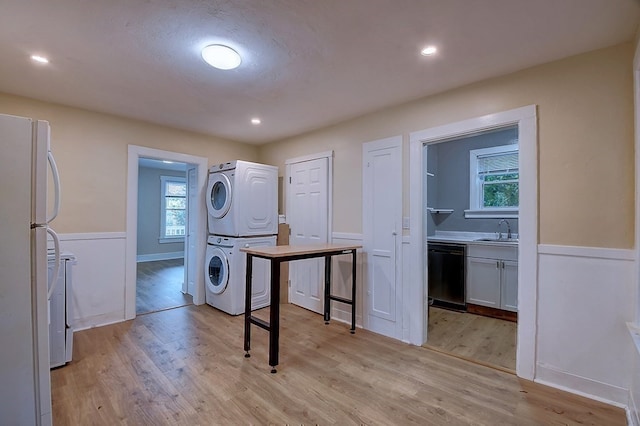 laundry room featuring stacked washing maching and dryer, sink, and light wood-type flooring