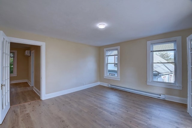 spare room featuring a wall mounted AC, light hardwood / wood-style floors, a wealth of natural light, and a baseboard heating unit