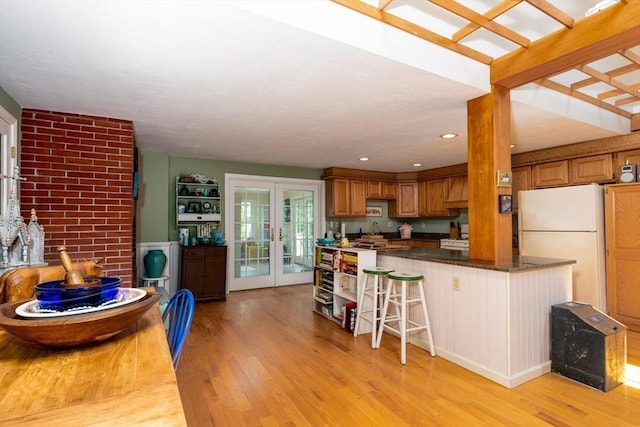 kitchen with white refrigerator, dark stone counters, french doors, light hardwood / wood-style floors, and a kitchen breakfast bar