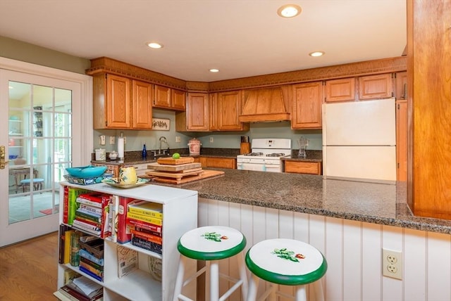 kitchen featuring premium range hood, white appliances, light wood-type flooring, dark stone counters, and sink